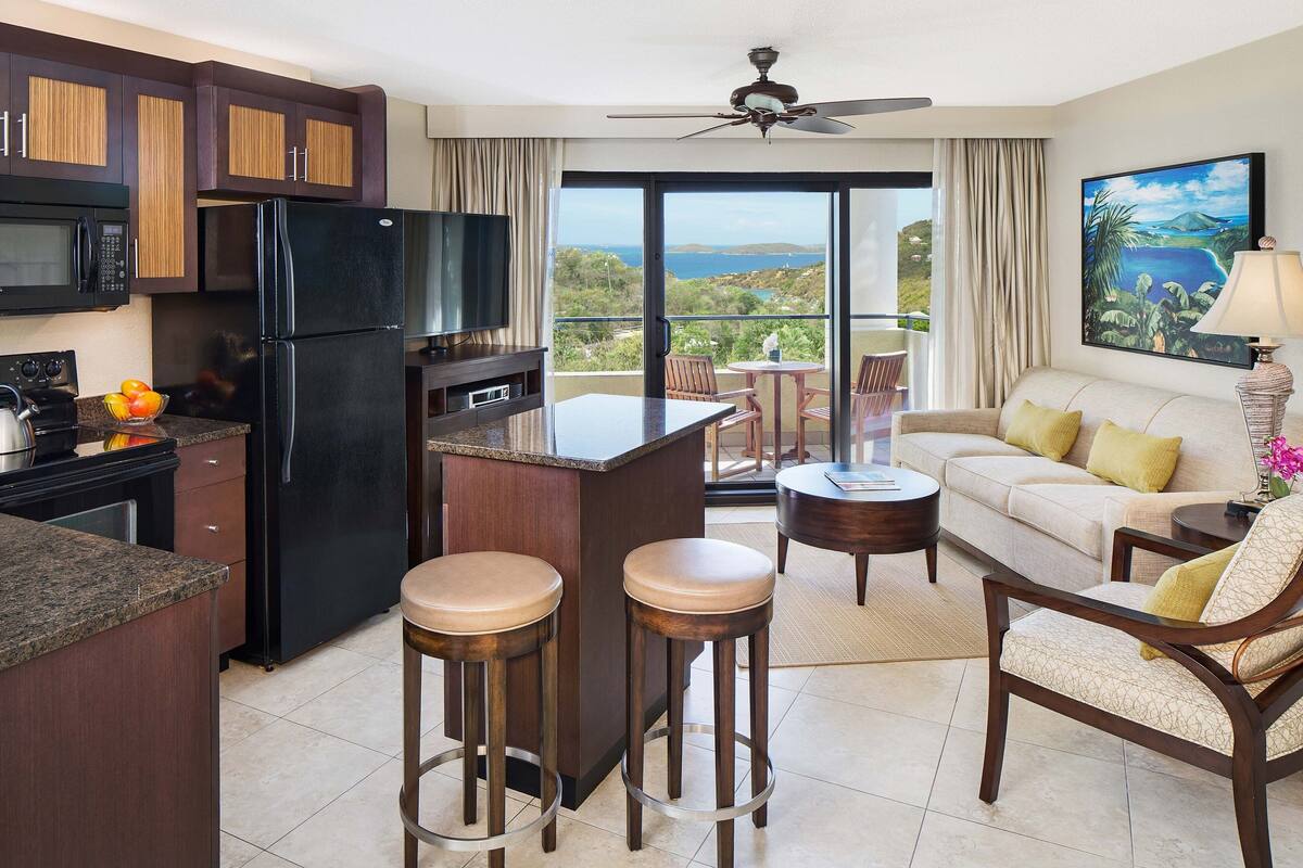 Una cocina moderna con un refrigerador negro, microondas y estufa, un comedor con una mesa redonda y sillas, y un balcón con vista al océano.