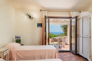 Un dormitorio con cama, mesita de noche, planta en maceta y vistas a un patio exterior con mesa y sillas.