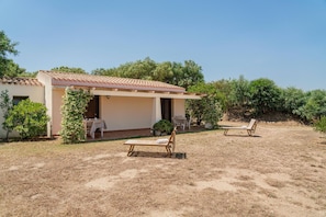 Una casa de dos pisos con un patio, dos sillones de madera y una mesa pequeña con mantel.