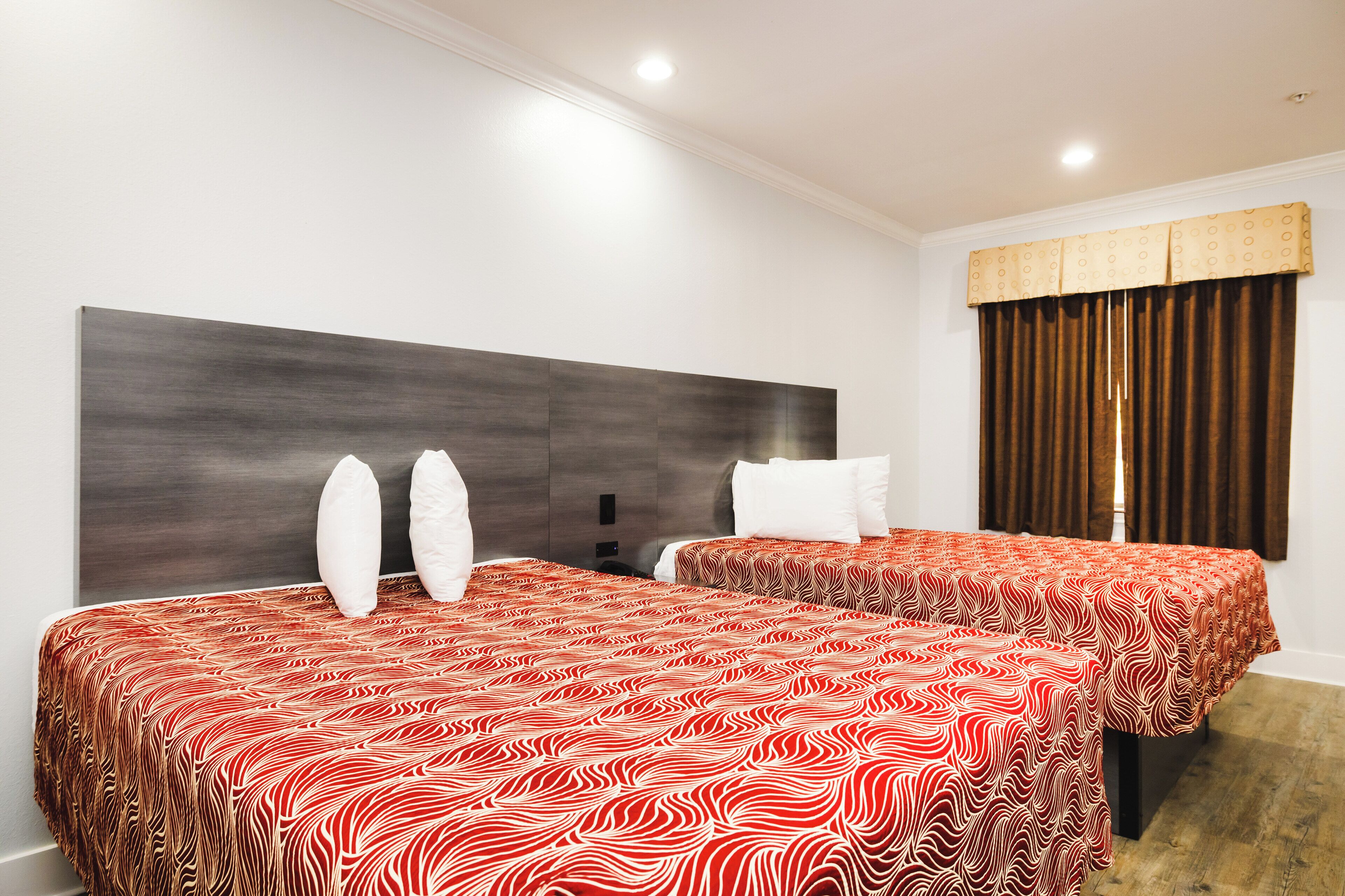 Habitación de hotel con dos camas, cada una con una colcha estampada, cabecero oscuro y ventana con cortinas marrones.