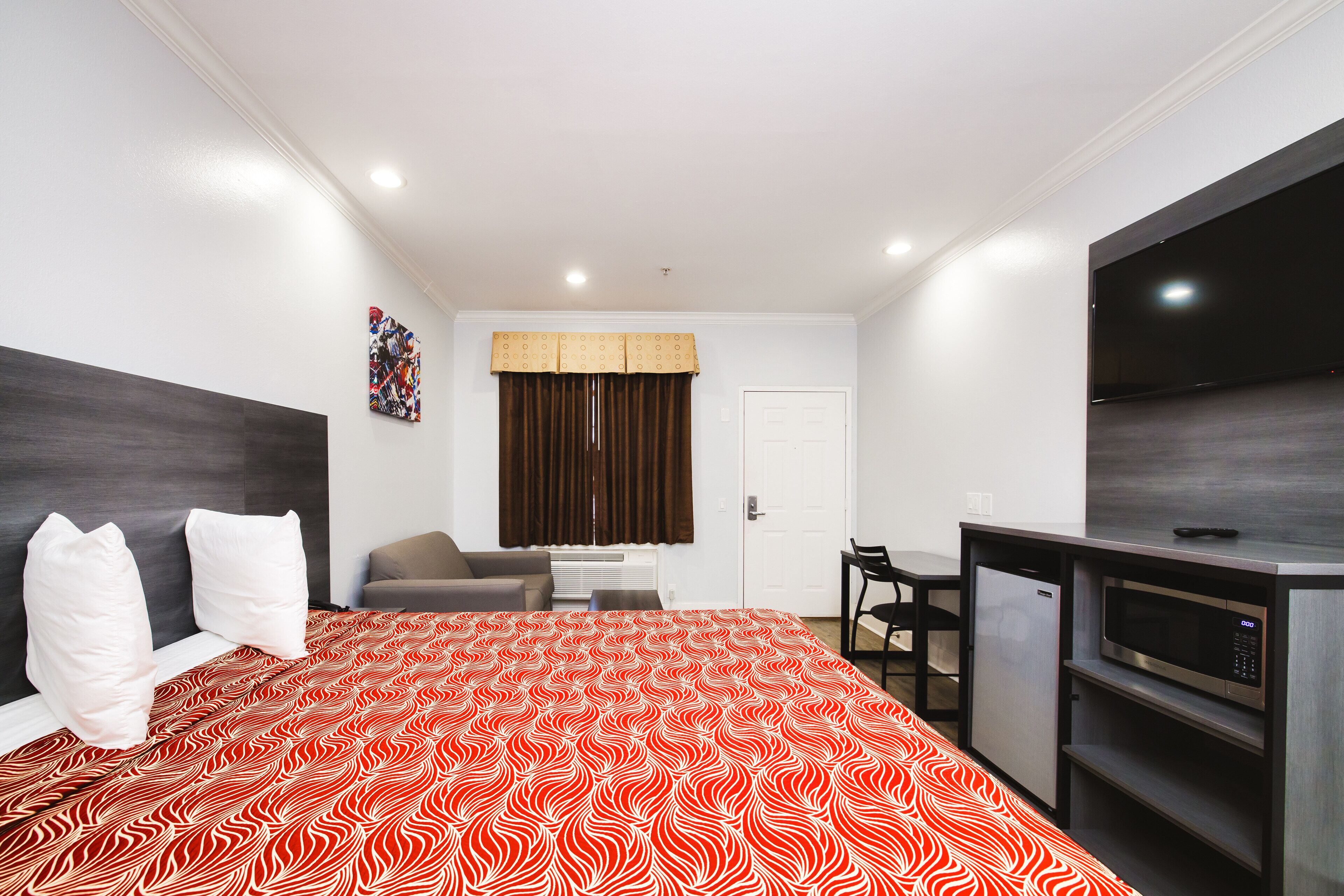Quarto de hotel com cama, escrivaninha, cadeira, micro-ondas e televisão.