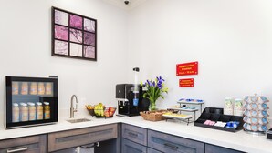 A modern kitchen with a coffee machine, fruit bowl, and breakfast sign. - Palace Inn Fairbanks (Houston)