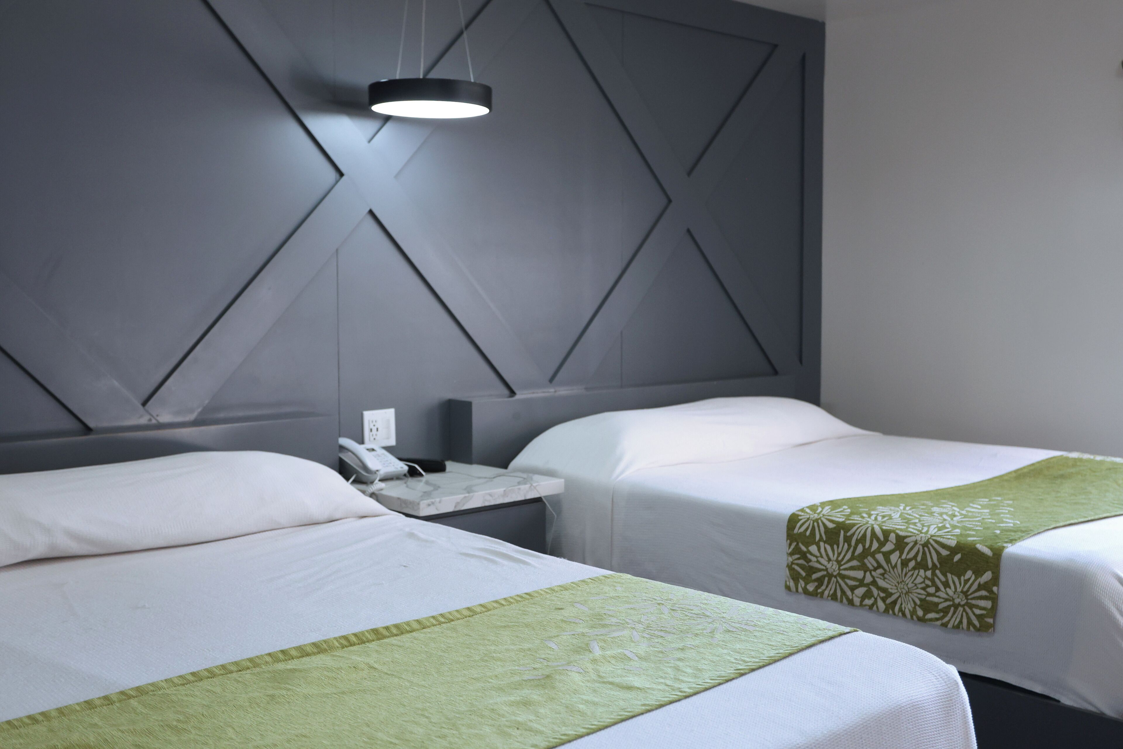 A hotel room with two beds, a nightstand, a modern light fixture, and a geometric-patterned headboard.