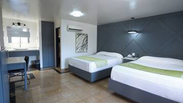 Una habitación de hotel con dos camas, un escritorio con silla, un espejo y un equipo de aire acondicionado.