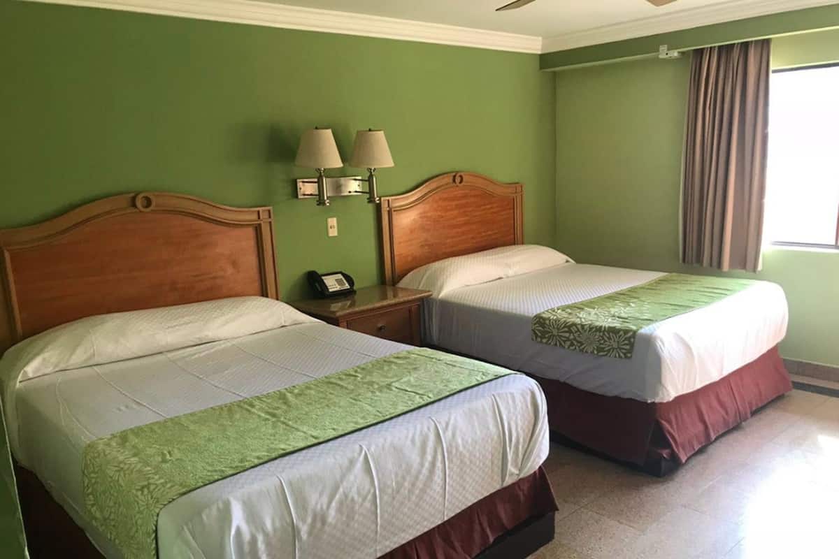 A hotel room with two beds, a nightstand with a phone, and a window with curtains.