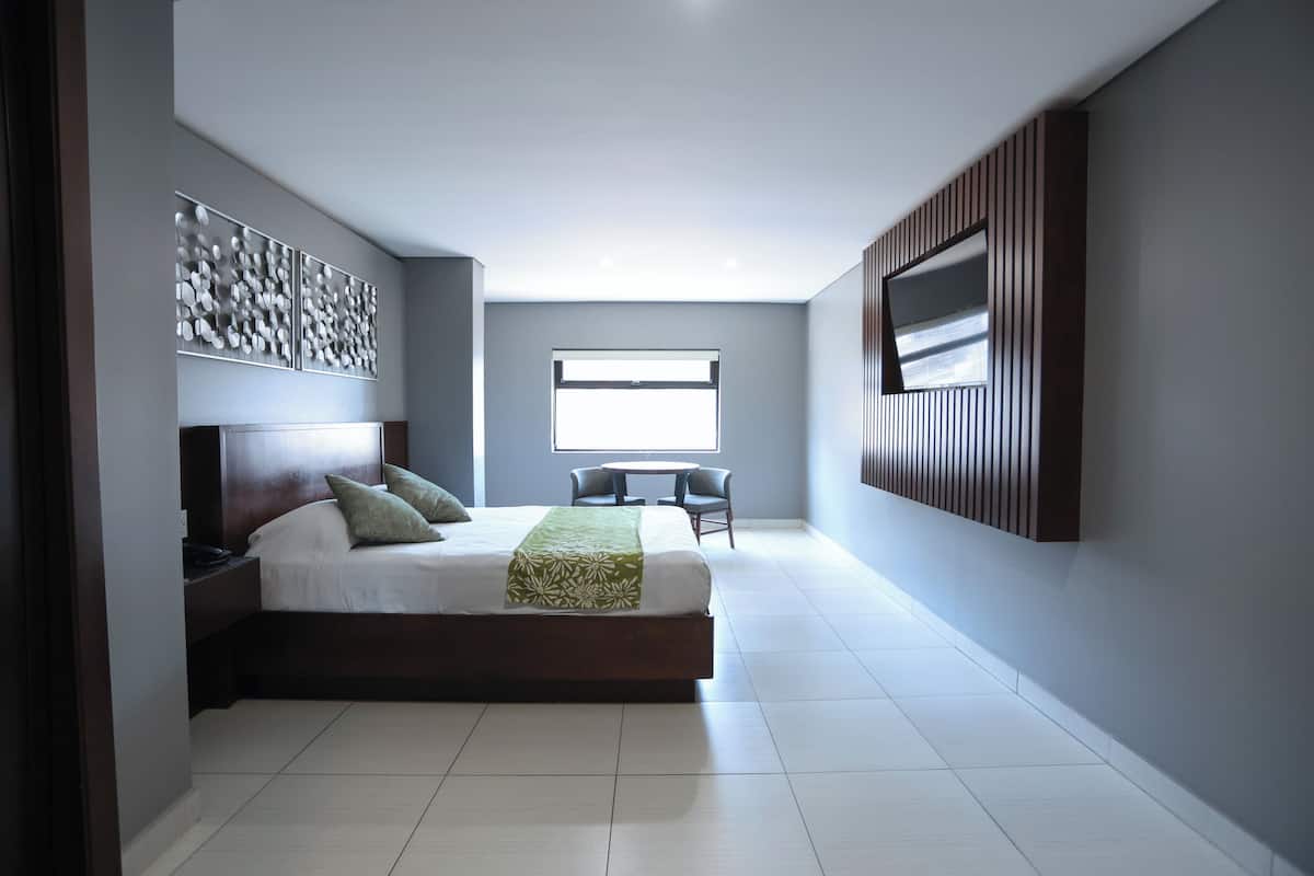 A modern bedroom with a large bed, a TV mounted on the wall, and a window providing natural light.