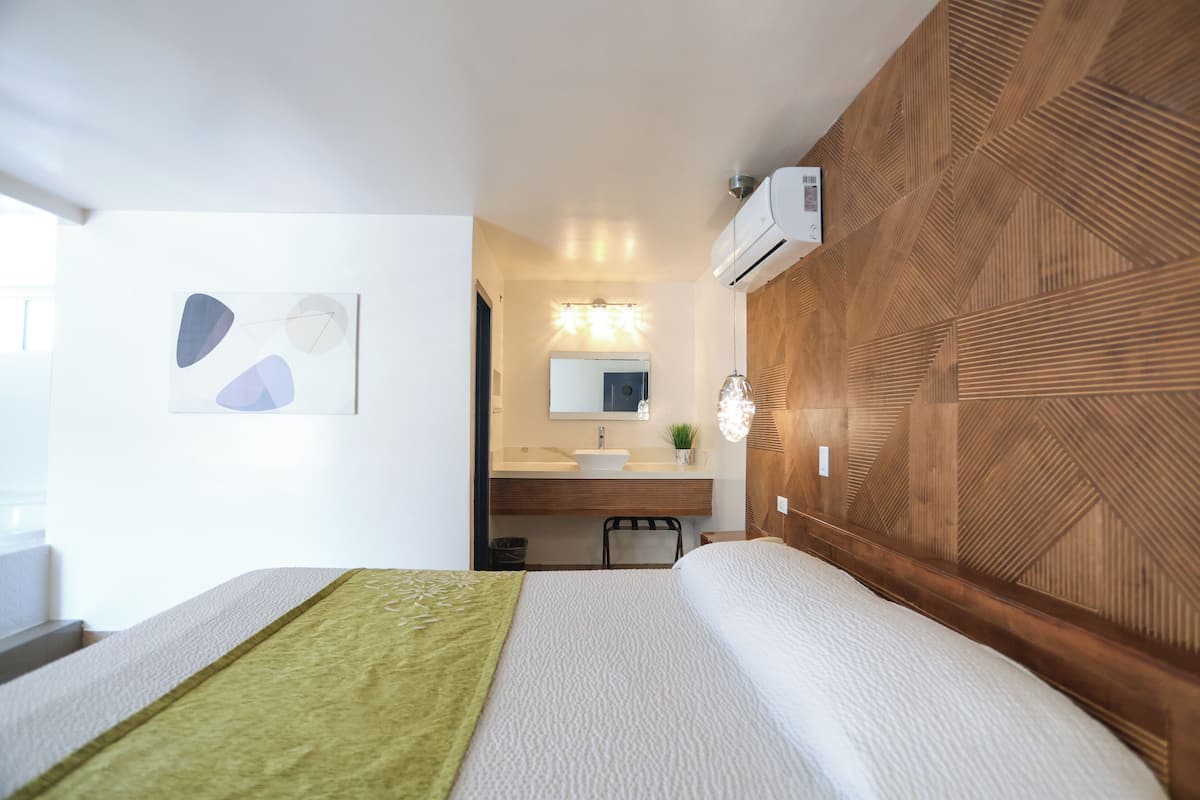 A modern hotel room with a bed, a bathroom with a sink and mirror, and a wooden accent wall.