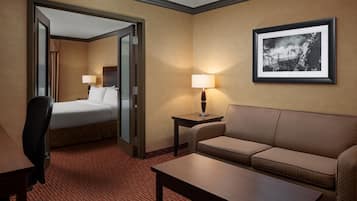 Quarto de hotel com cama, sofá, escrivaninha, luminária e quadro na parede.
