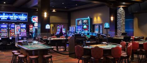 A casino with multiple blackjack tables, slot machines, and a neon-lit sign for 'Hotel'.