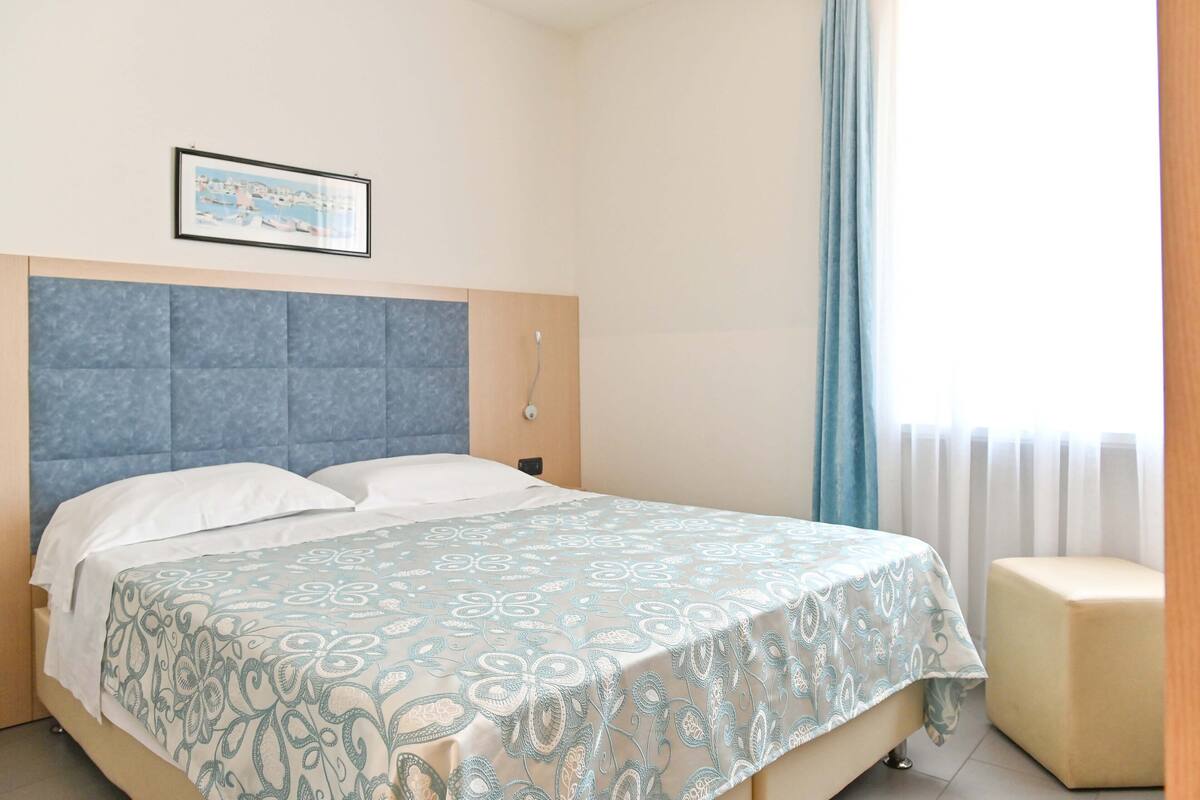 A neatly made bed with a patterned bedspread, a headboard, and a bedside table with a lamp.
