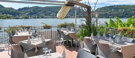 An outdoor dining area with tables and chairs, overlooking a lake with hills in the background.