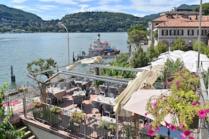 A riverside restaurant with outdoor seating, a dock with a boat, and a mountainous backdrop. - Hotel Marco's (Como)