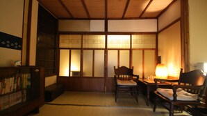 A traditional Japanese room with tatami flooring, a low table with chairs, a bookshelf, and sliding doors with shoji screens. - HARUYA Higashiyama - Hostel (Kyoto)
