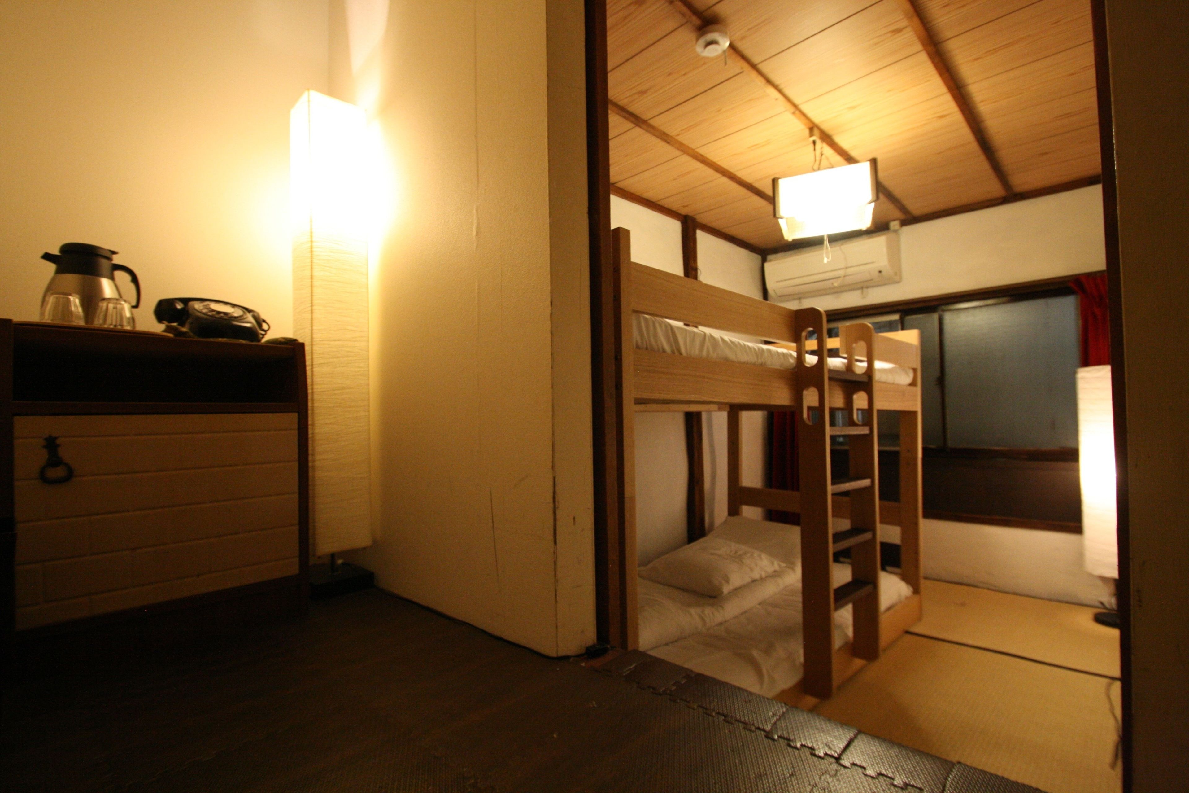 Quarto compacto com beliche, uma pequena escrivaninha com luminária e ar condicionado fixado na parede.
