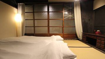 A traditional Japanese-style room with tatami flooring, a low wooden bed, sliding shoji doors, and a dark wooden dresser.
