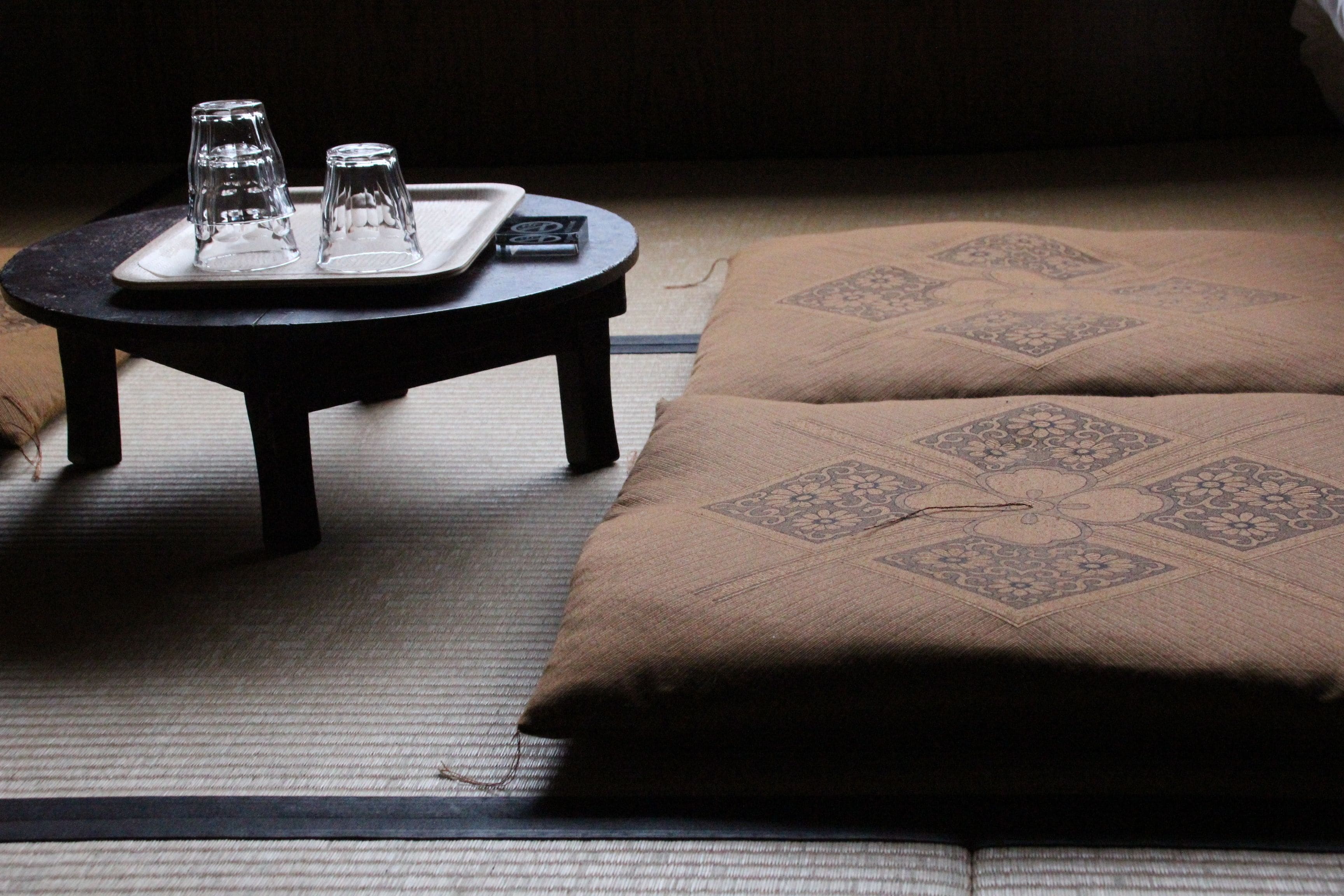 A tatami mat room with a low table, two glasses, and a remote control.