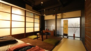 A traditional Japanese room with tatami flooring, a low table, cushions, and sliding doors. - HARUYA Higashiyama - Hostel (Kyoto)