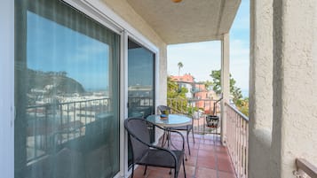 Enjoy the breathtaking view of the coastal city from this balcony with a sliding glass door, round table, and comfortable seating for two.