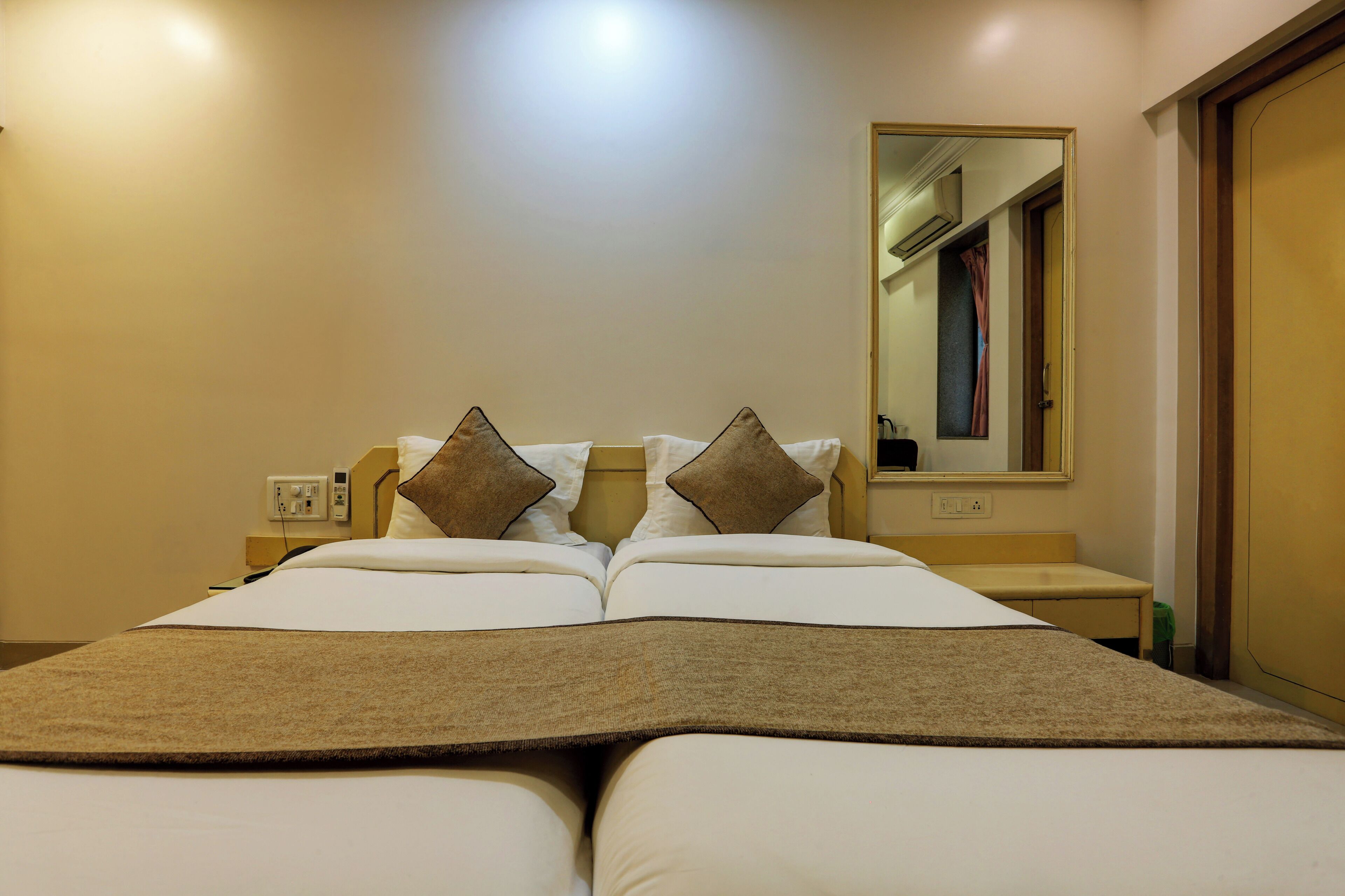 A hotel room with a large bed, two pillows, a bedside table, a mirror, and a door.