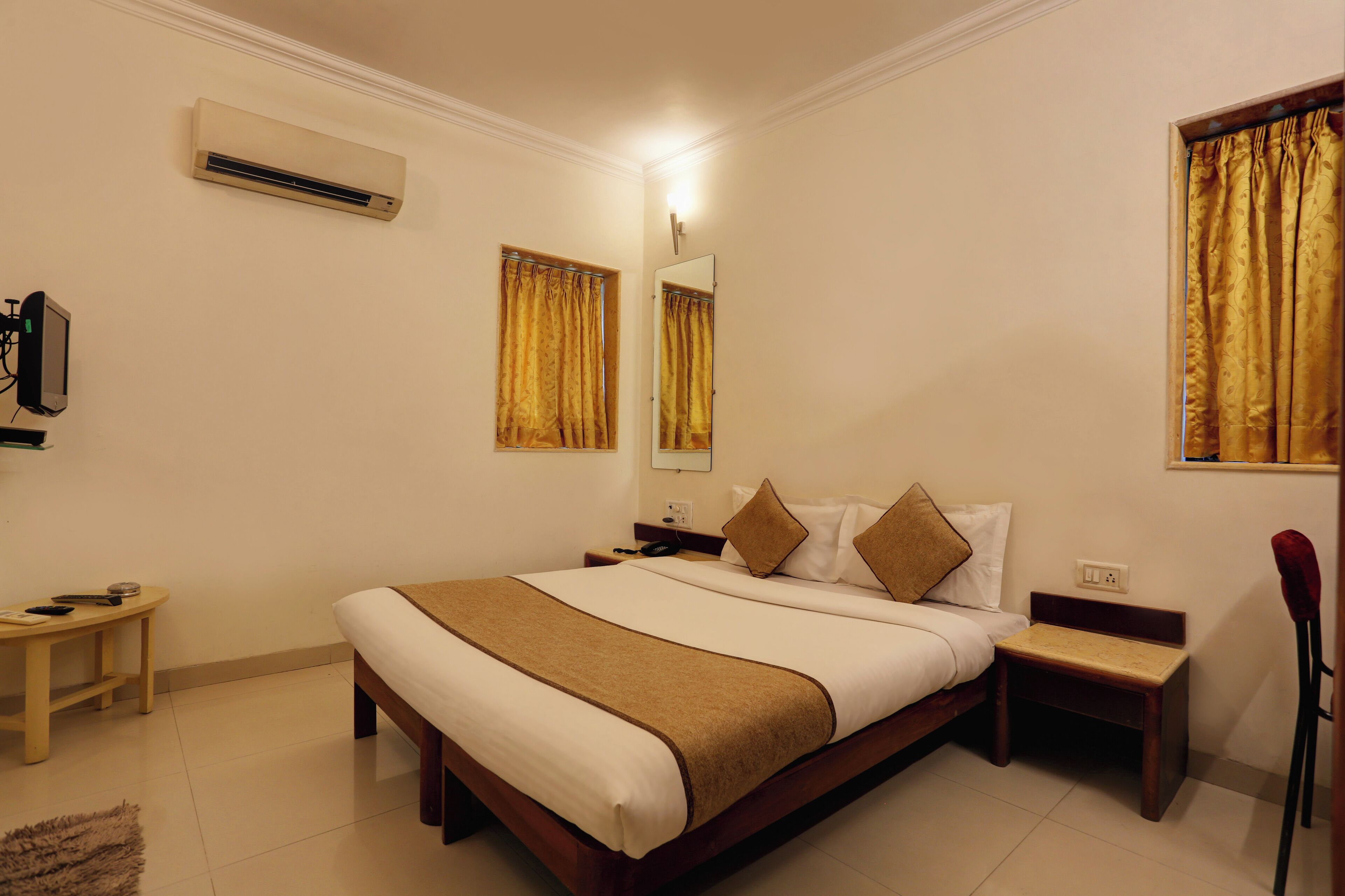 A hotel room with a large bed, bedside tables, an air conditioning unit, a mirror, and curtains.