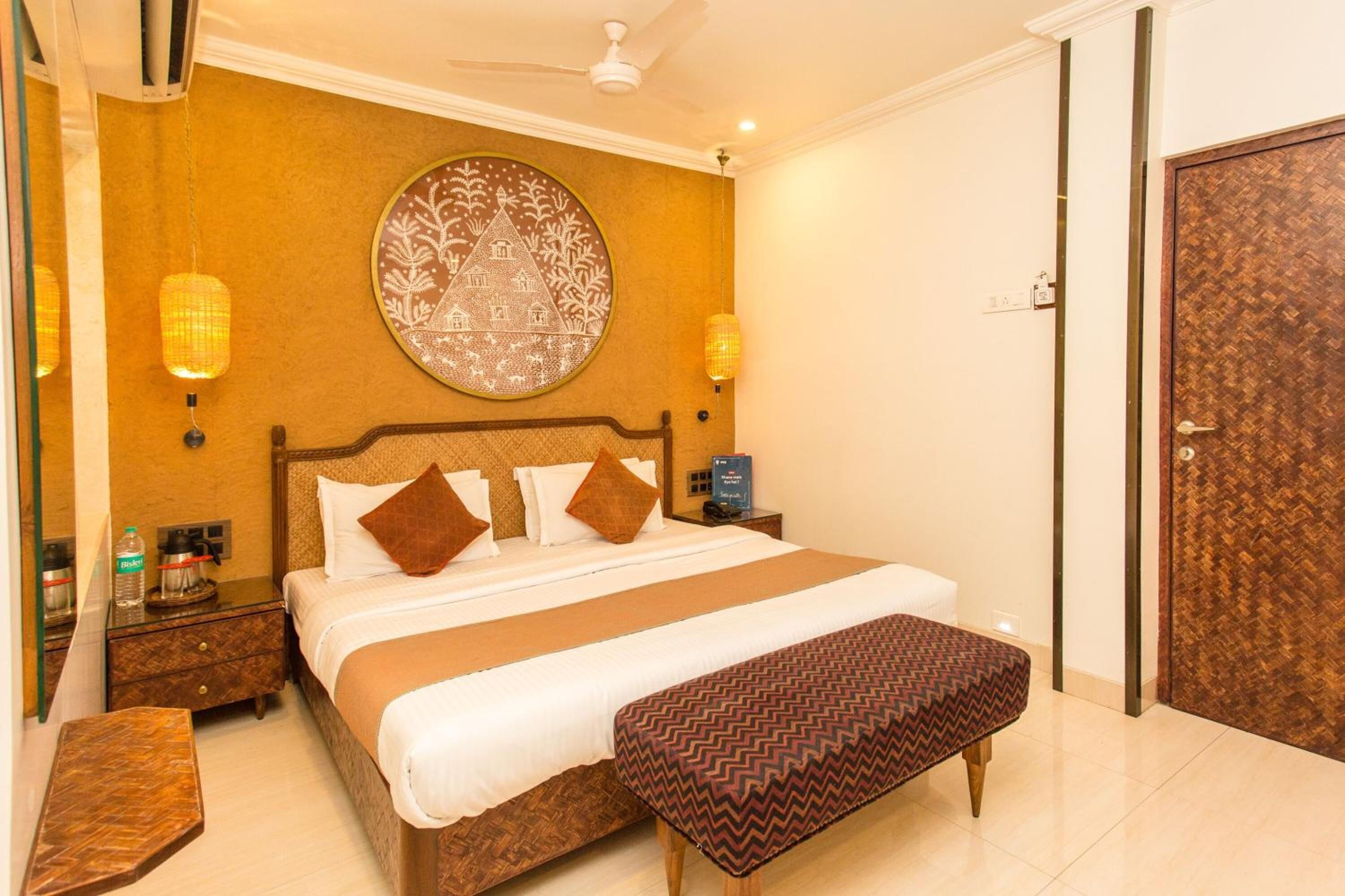 Habitación de hotel con una cama grande, una mesita de noche con una botella, un adorno circular en la pared y una puerta de madera.