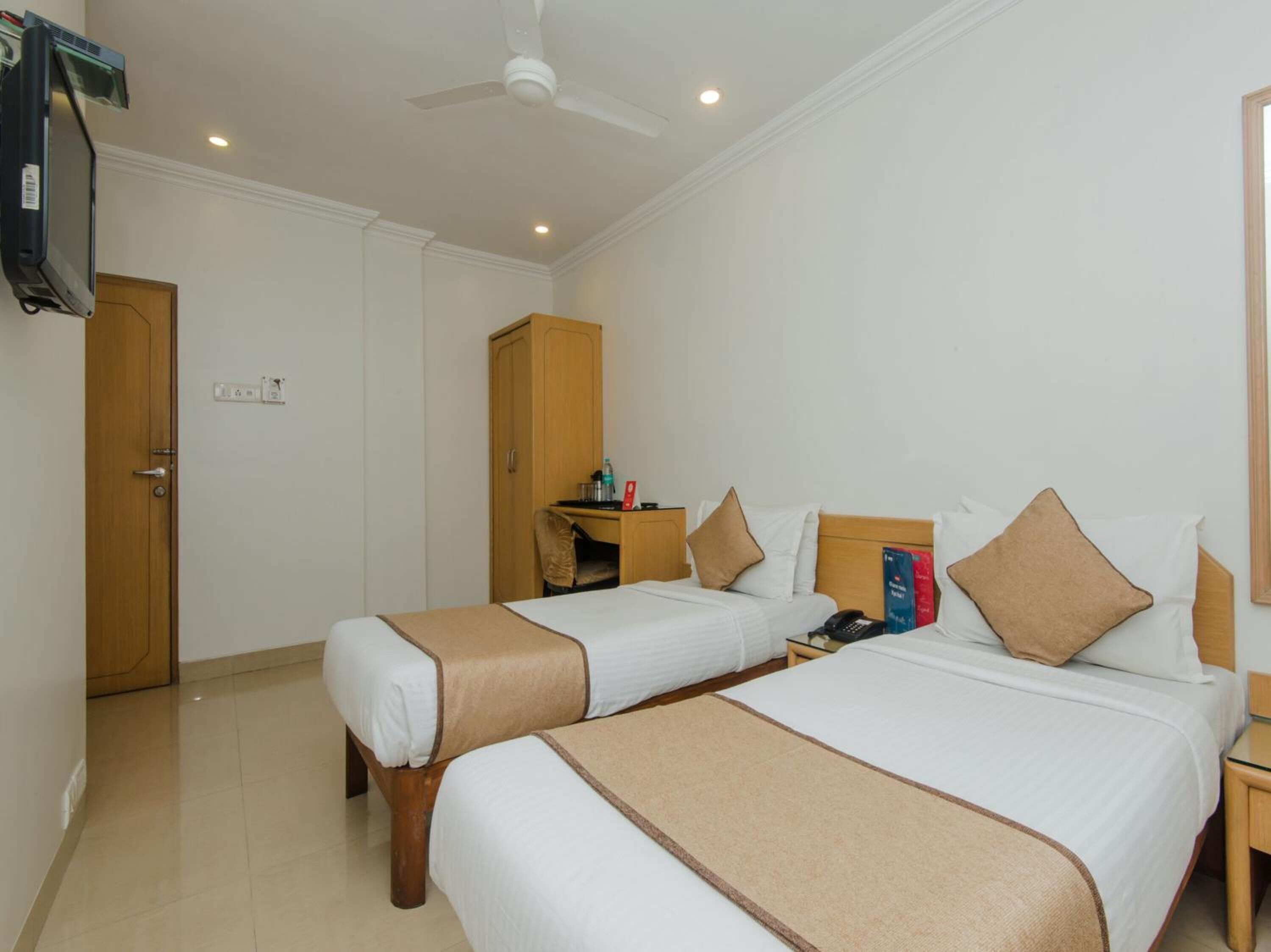 Habitación de hotel con dos camas, un escritorio, un armario y un ventilador de techo.