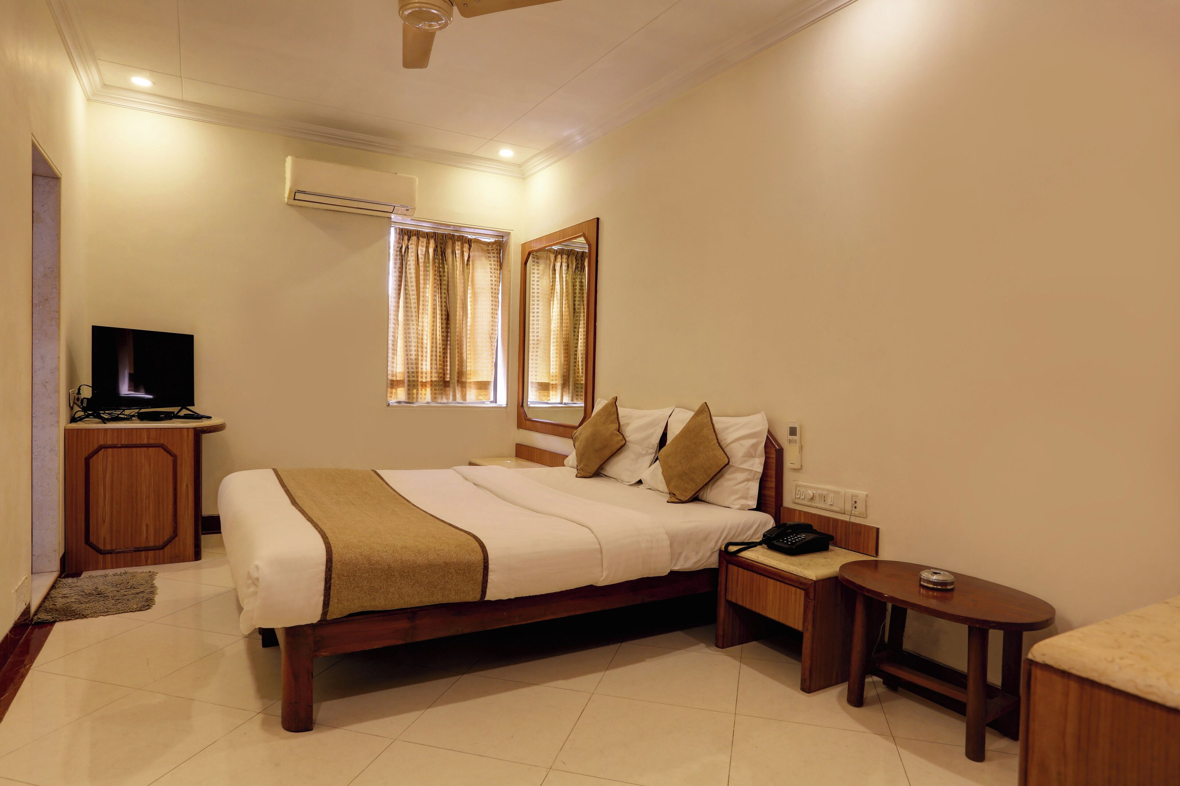 A hotel room with a bed, bedside table, TV, and a window with curtains.