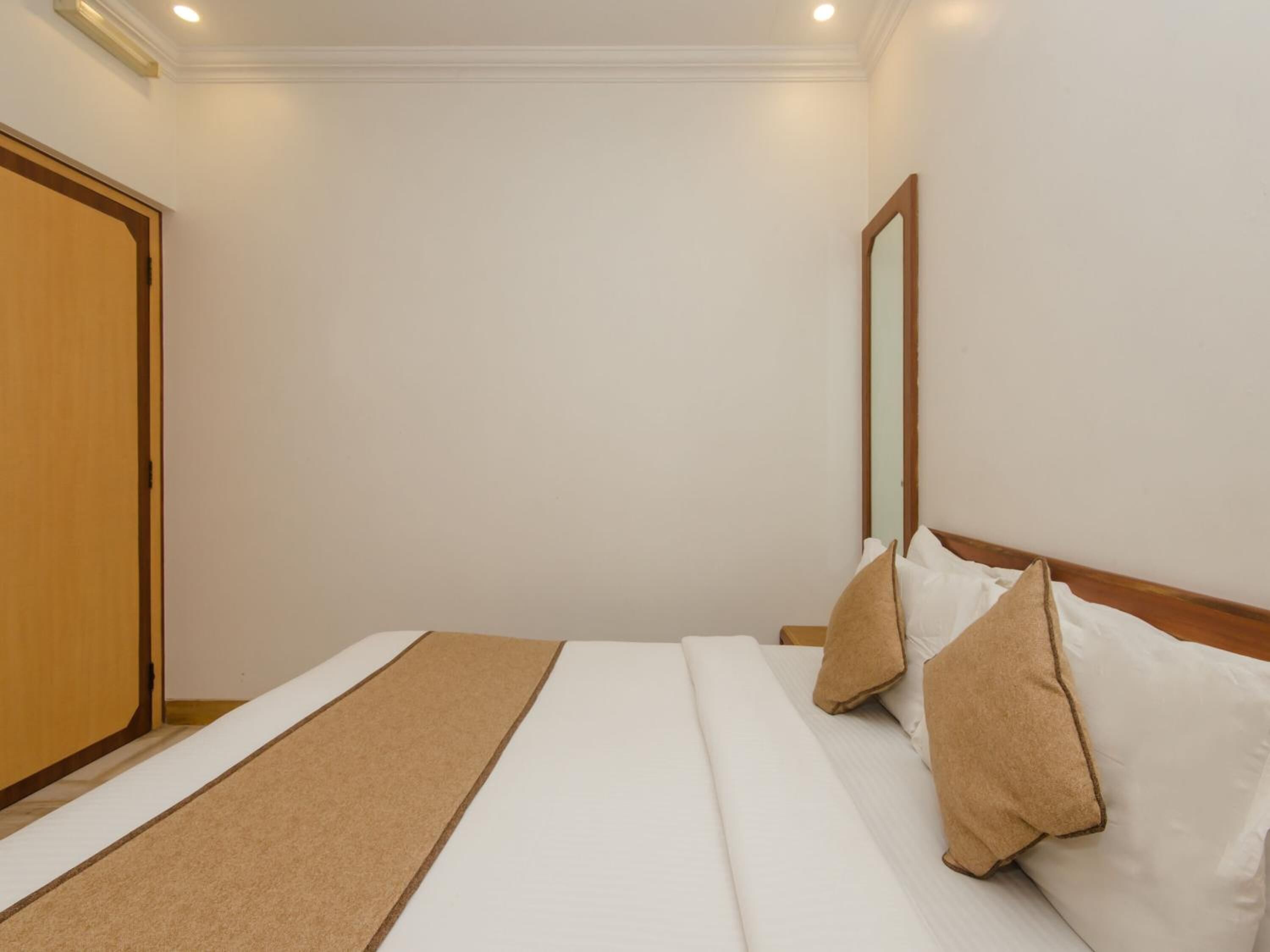 Quarto de hotel com cama, porta de madeira, espelho e tapete marrom.