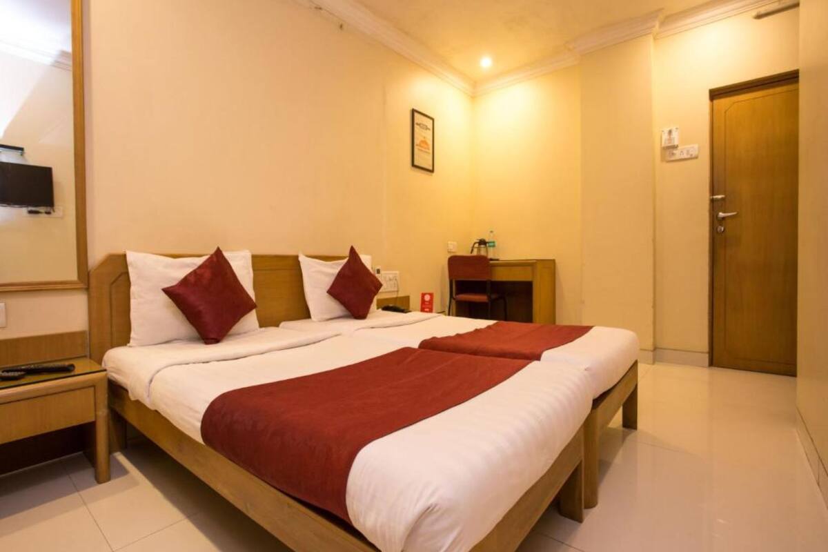 A hotel room with a double bed, a desk, a chair, a TV, and a door.