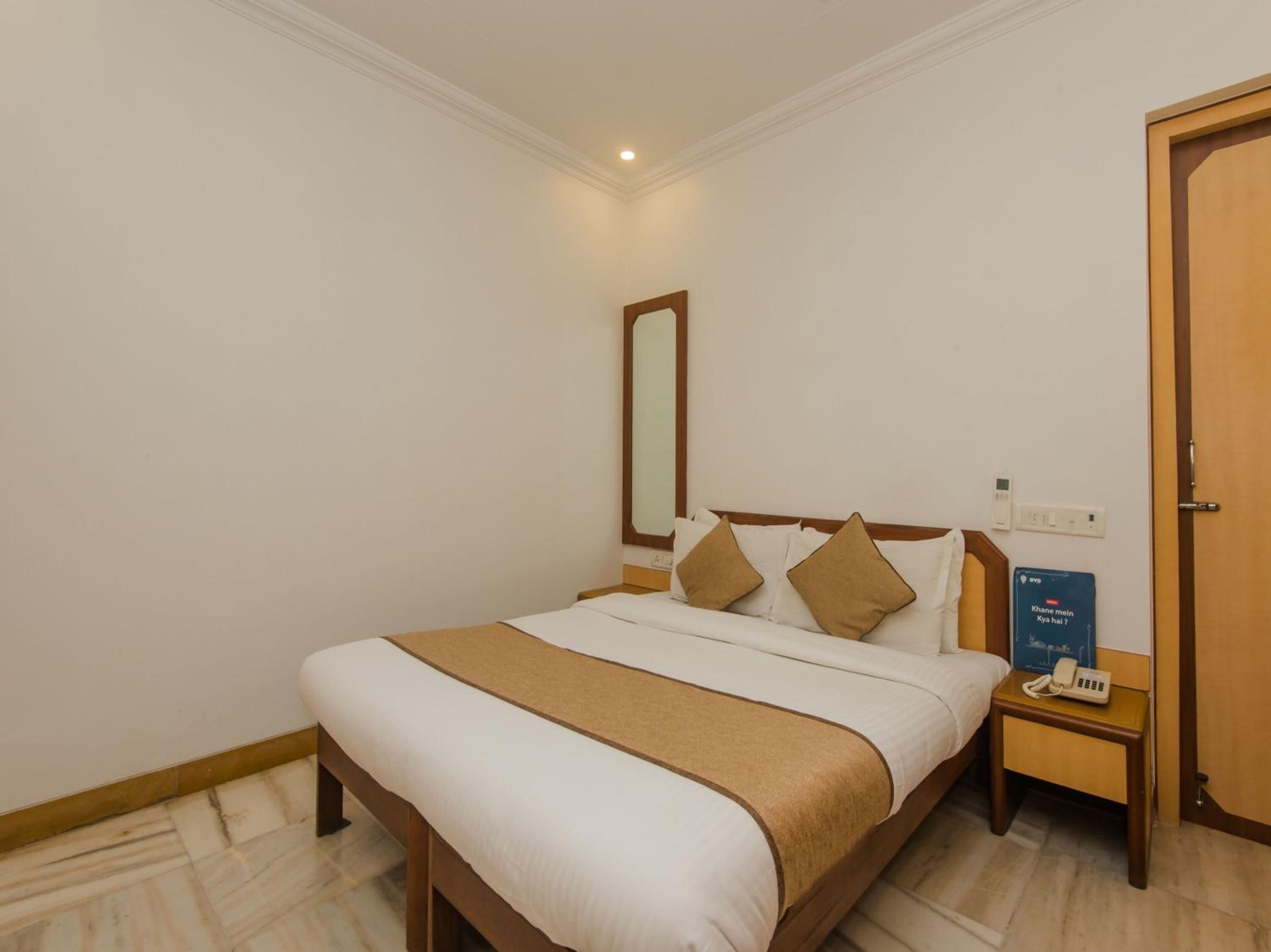 A hotel room with a bed, bedside tables, a mirror, a door, and a sign with text.