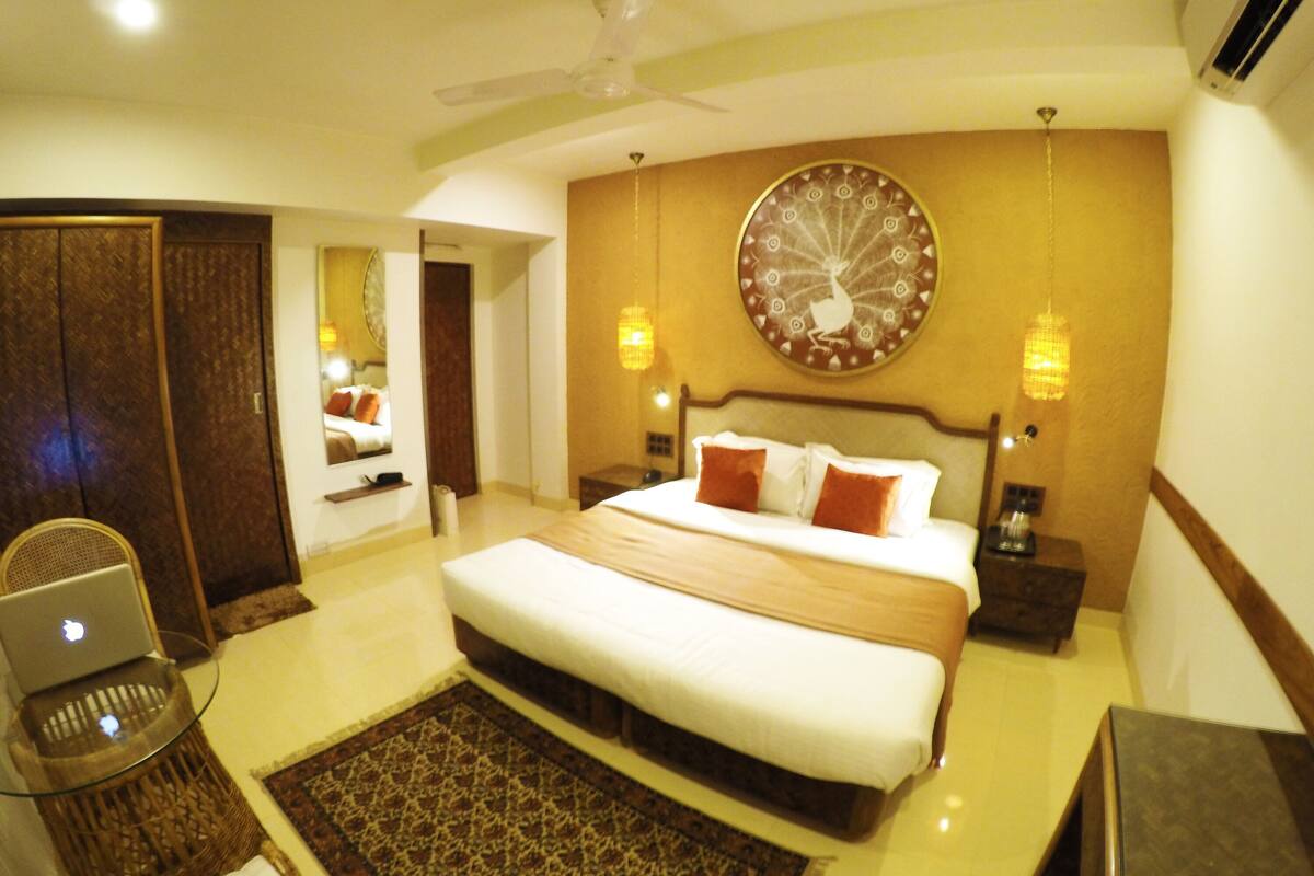 A hotel room with a large bed, a desk with a laptop, a wall clock, and a decorative wall piece.