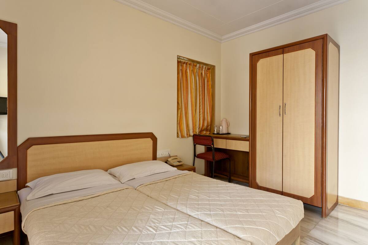 A hotel room with a bed, a desk, a wardrobe, and a mirror.