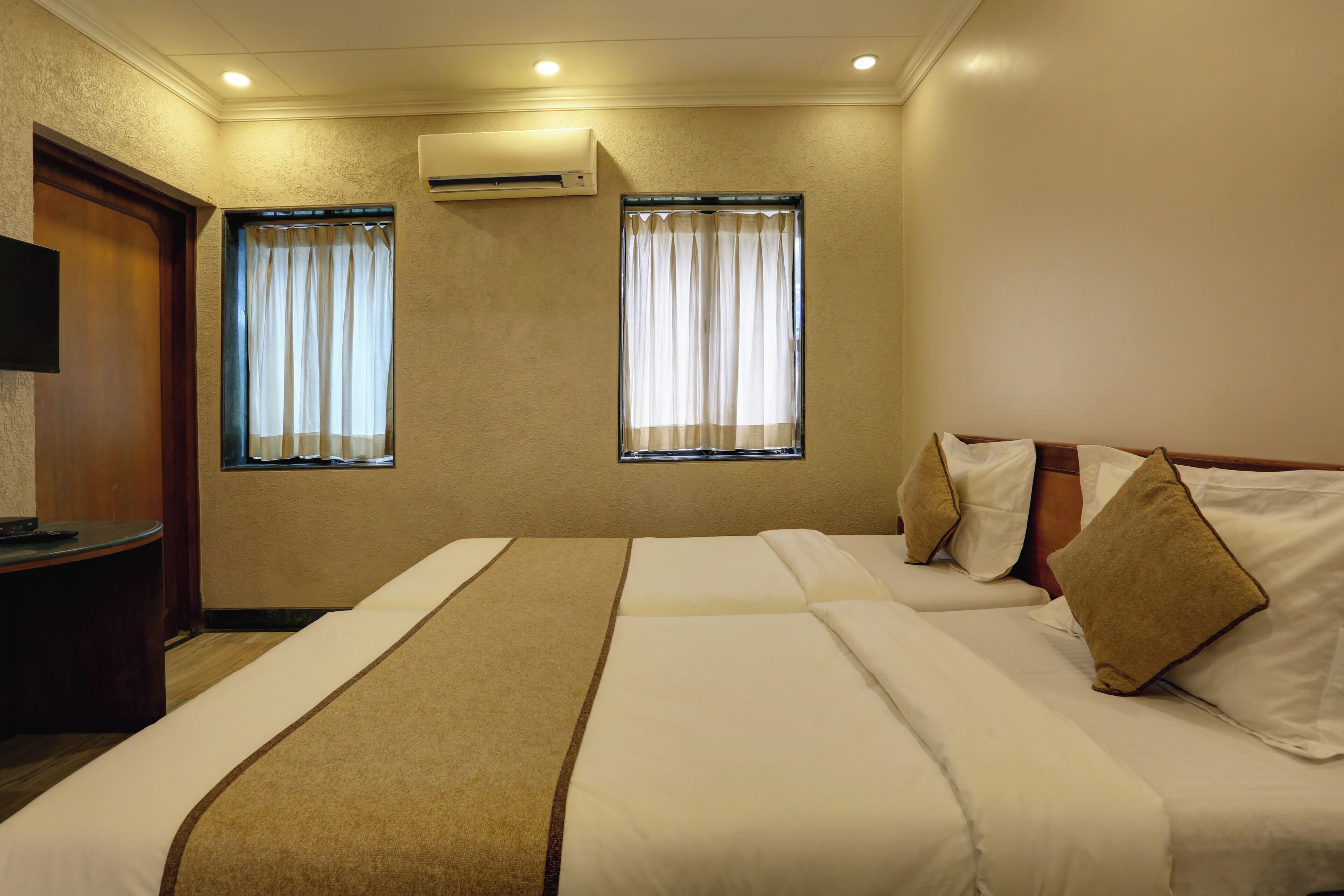 Una habitación de hotel con dos camas, un escritorio de madera y dos ventanas con cortinas.