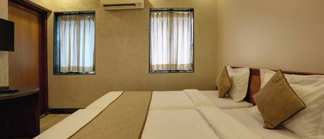 A hotel room with two beds, a wooden desk, and two windows with curtains.