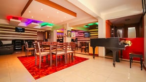 A hotel lobby with a dining area, a piano, and a TV screen. - Nairobi Upperhill Hotel (Nairobi)
