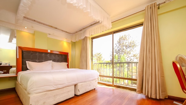 A spacious bedroom with a large bed, a balcony view, and a wooden floor. - Nairobi Upperhill Hotel (Nairobi)