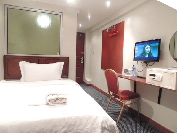 A hotel room with a bed, a desk with a television, a chair, and a microwave.