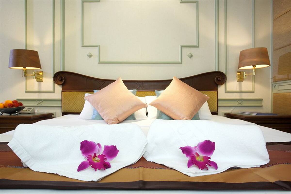 Une chambre d’hôtel avec un lit bien fait, deux oreillers, une table de chevet avec une lampe et un panier de fruits.