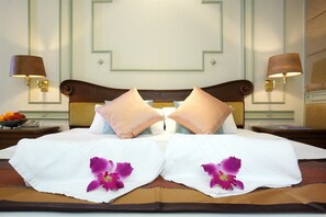 A hotel room with a neatly made bed, two pillows, a nightstand with a lamp, and a fruit bowl.