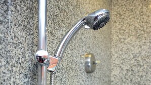 A shower with a chrome head and hose, mounted on a textured wall. - Majestic Suites (Bangkok)