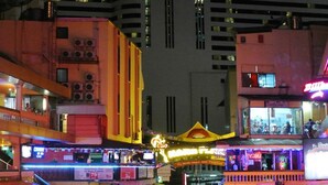 A brightly lit urban area with a prominent yellow building featuring multiple air conditioning units. - Majestic Suites (Bangkok)