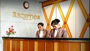 A reception desk with a sign that reads "RECEPTION" and a clock above it. - Majestic Suites (Bangkok)
