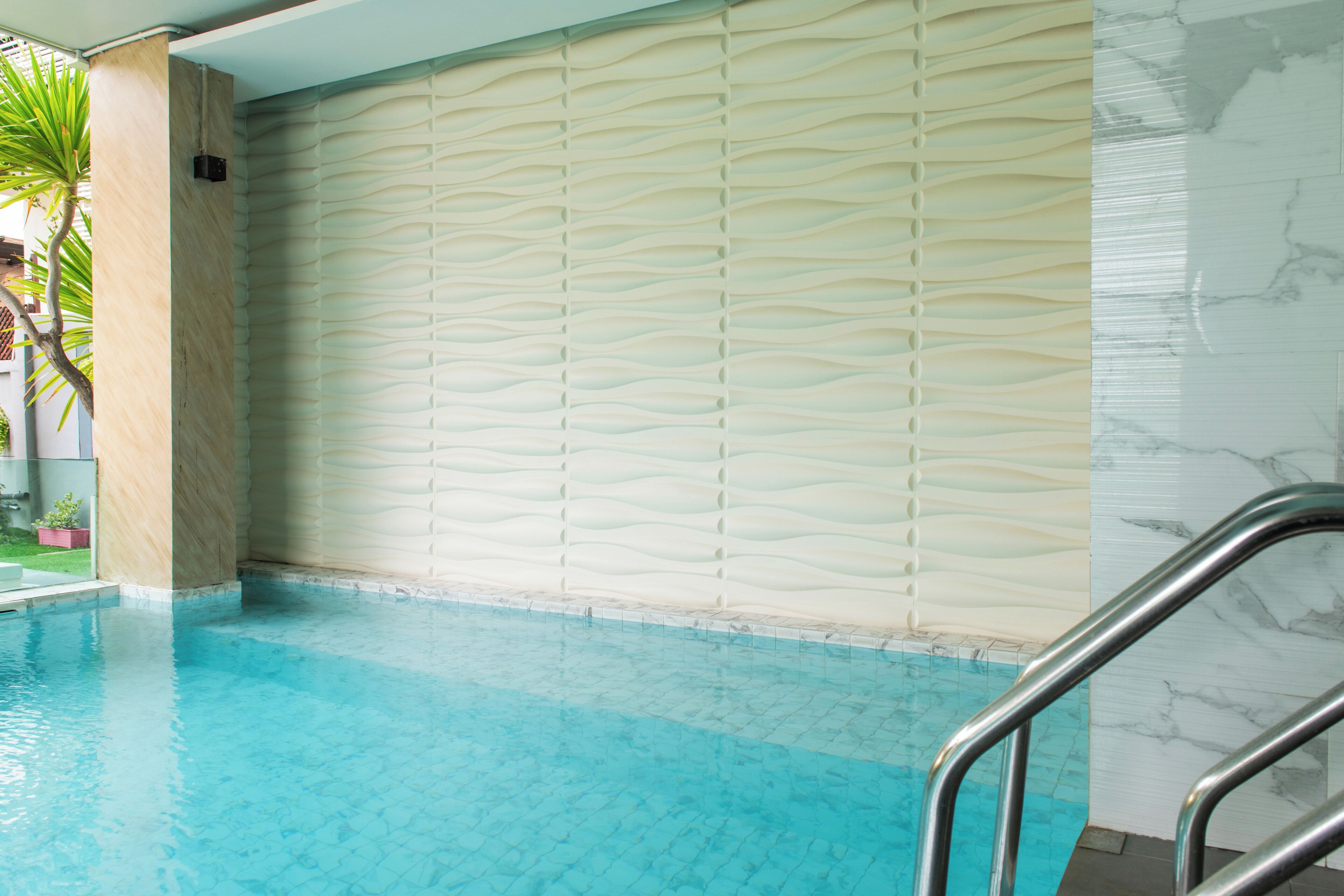Ein überdachter Pool mit wellenförmiger Wandgestaltung, klarem blauen Wasser und einer Metallleiter.