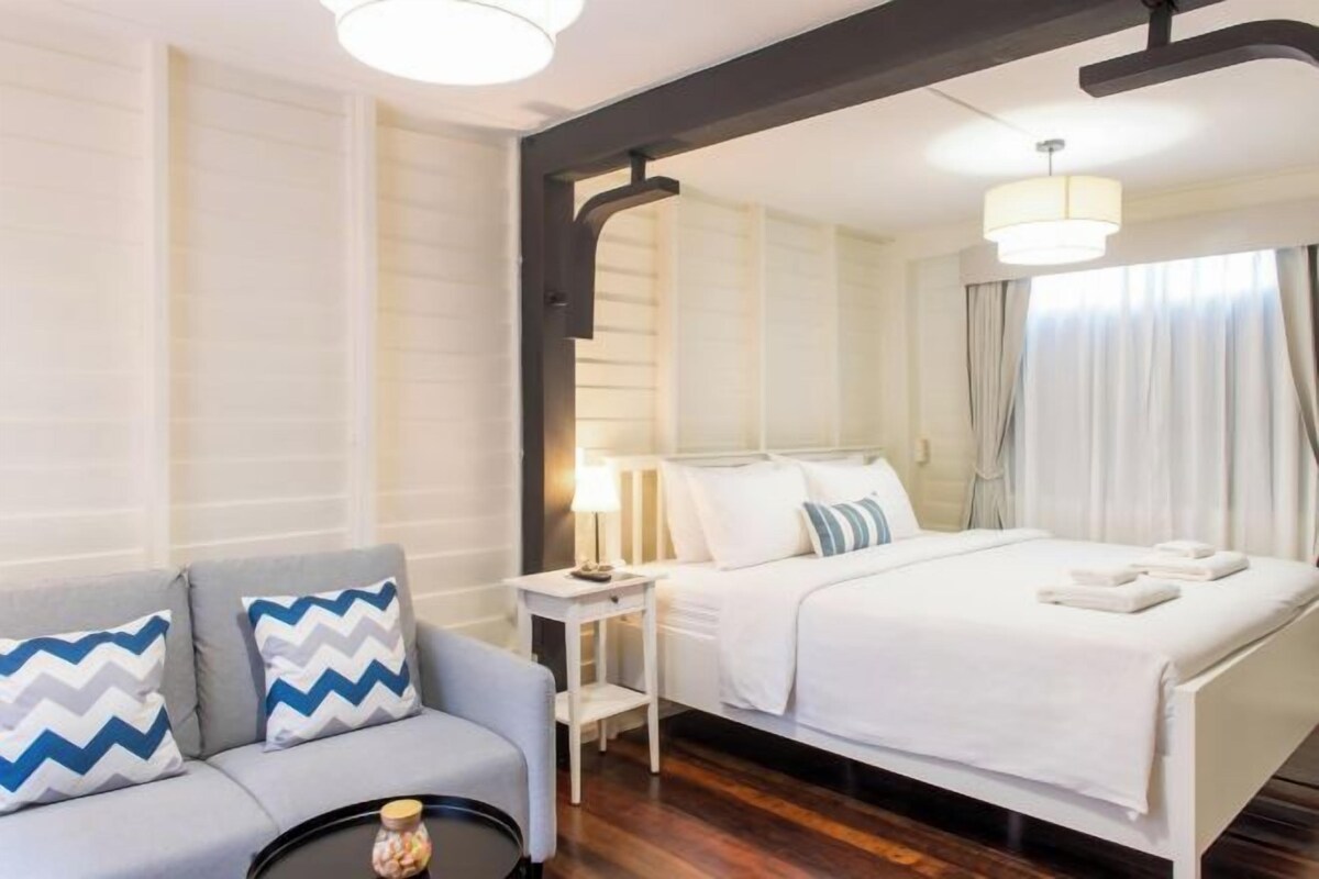A hotel room with a bed, a nightstand, a lamp, a sofa, and a mirror.