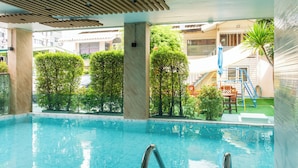 An indoor swimming pool with clear water, surrounded by greenery and a view of residential buildings. - Resort Bangphlat (Bangkok)