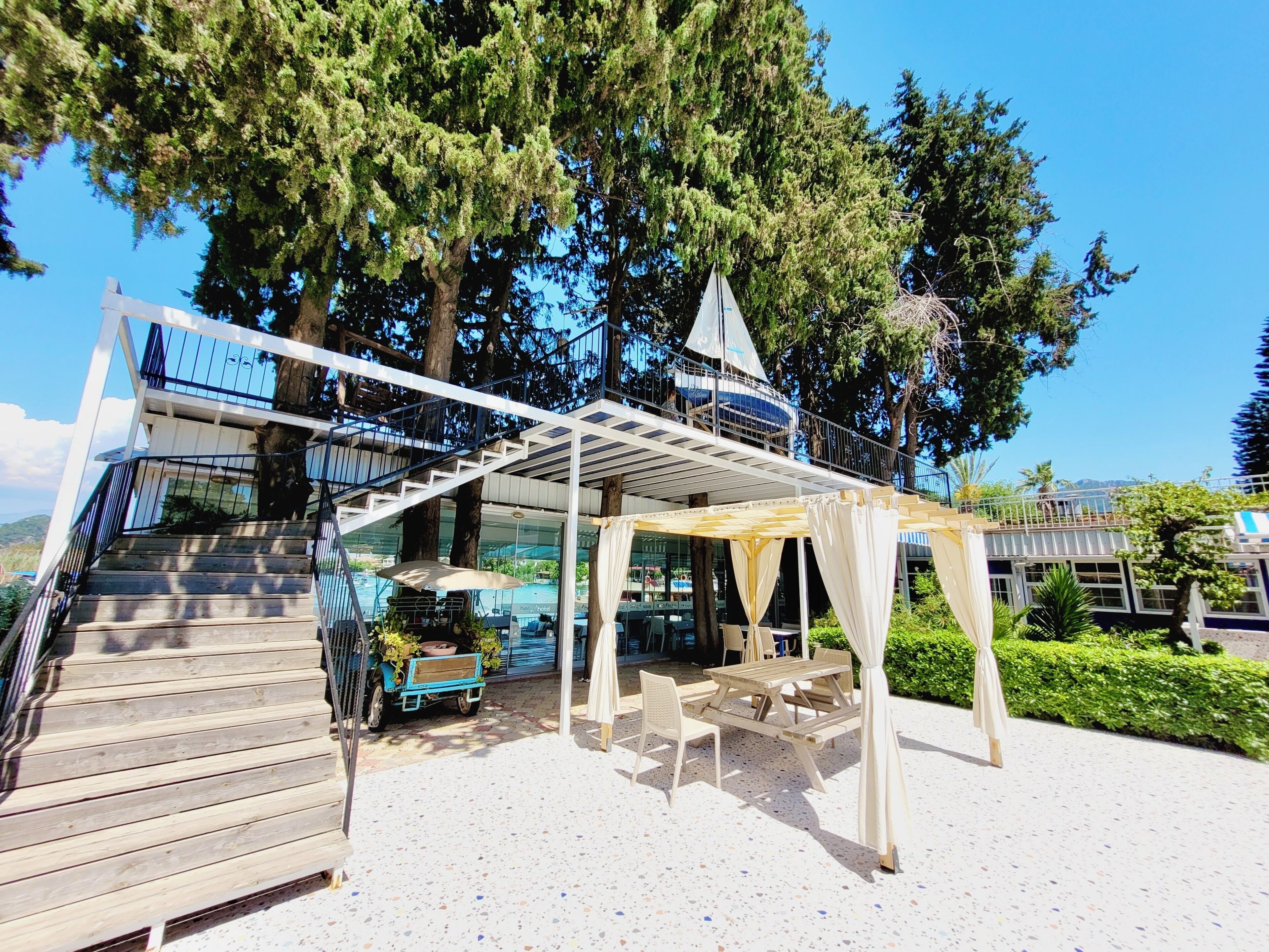A covered outdoor seating area with a table and chairs, a blue cart, and a staircase leading to an upper level.