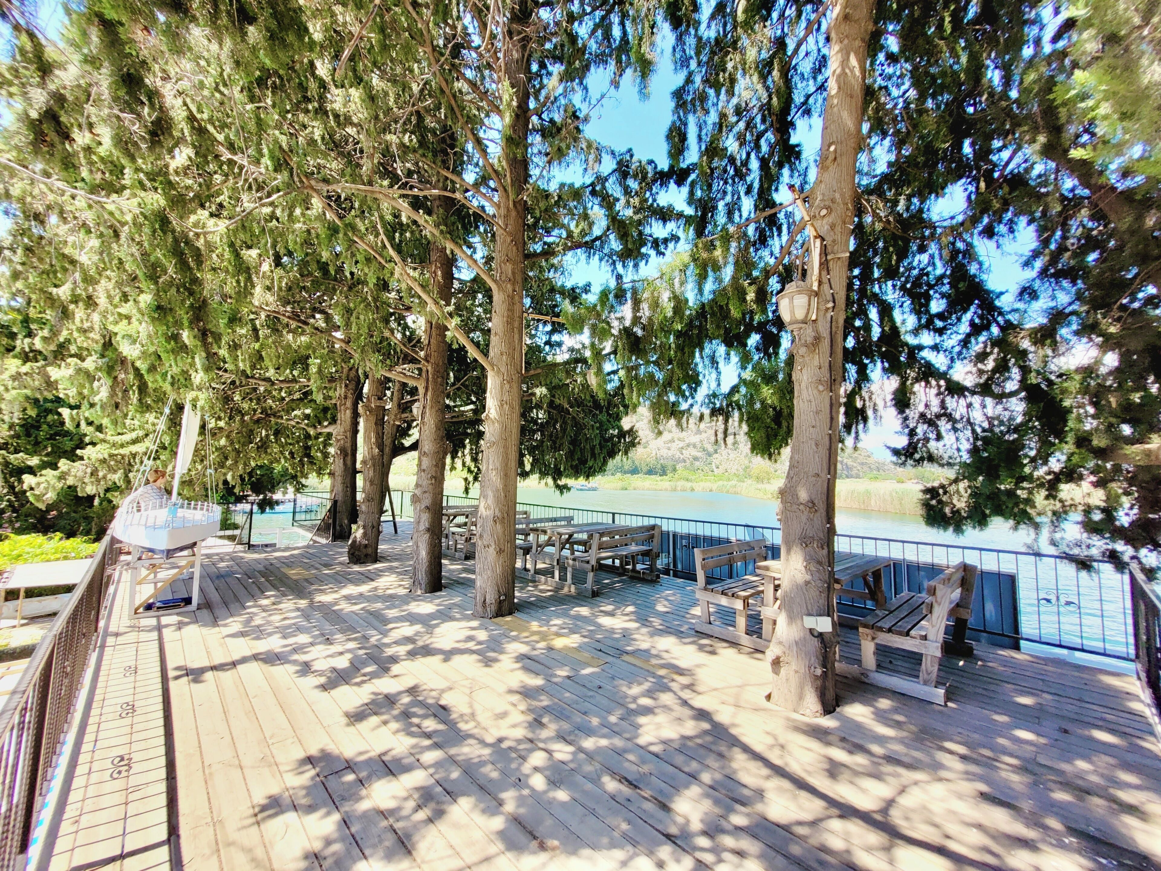 Terraza de madera con bancos y mesas, con vista a un cuerpo de agua.