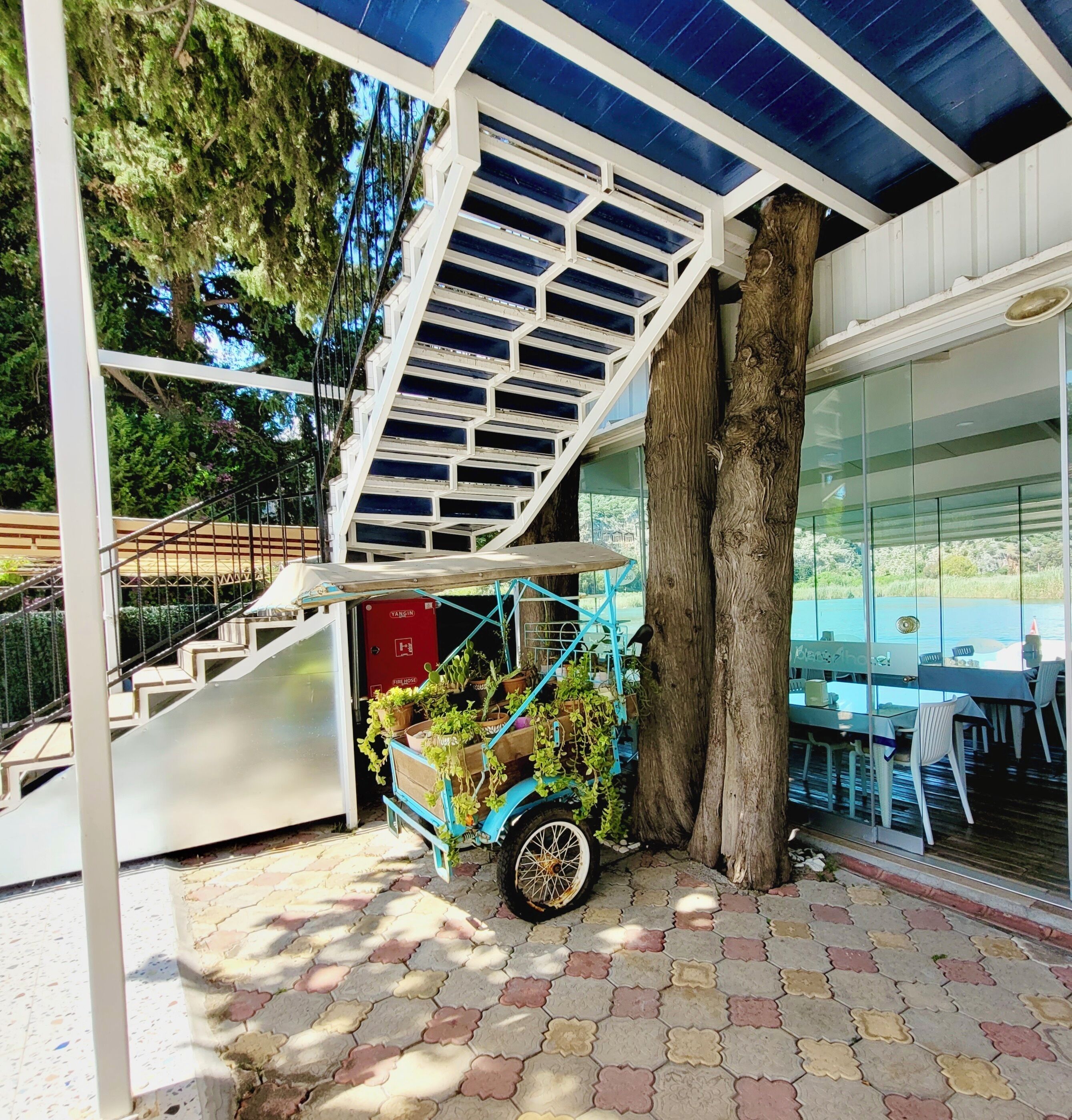 Un espacio al aire libre techado con una escalera, un carrito con plantas y un hidrante.