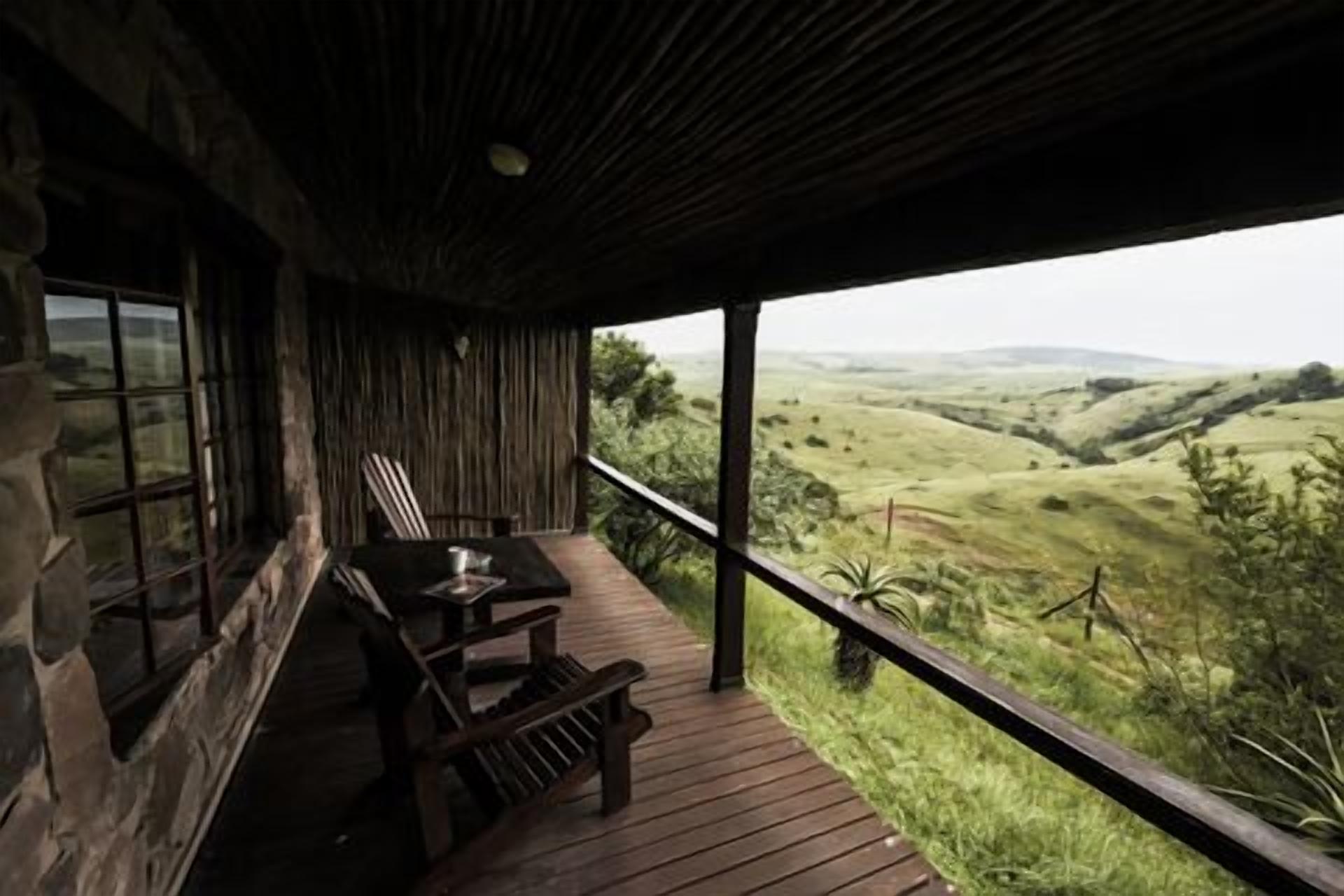 A wooden deck with a table and chairs, overlooking a hilly landscape.