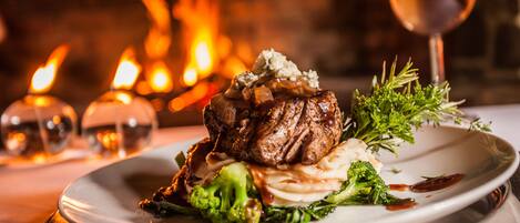 Un plato de comida con un bistec, brócoli y decoración, sobre un fondo con una chimenea encendida.